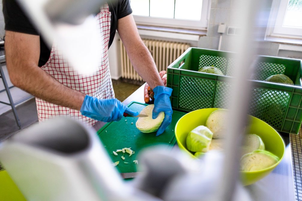 Hände in Handschuhen schneiden Weißkohl auf einem grünen Brett